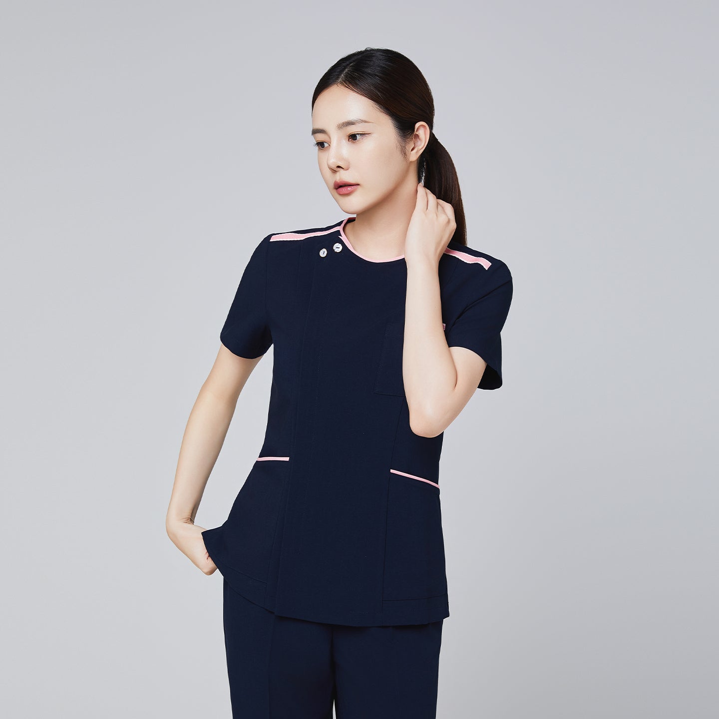Image of Navy scrub top with pink accents and a modern design, featuring a front pocket and short sleeves, modeled by a woman,Navy