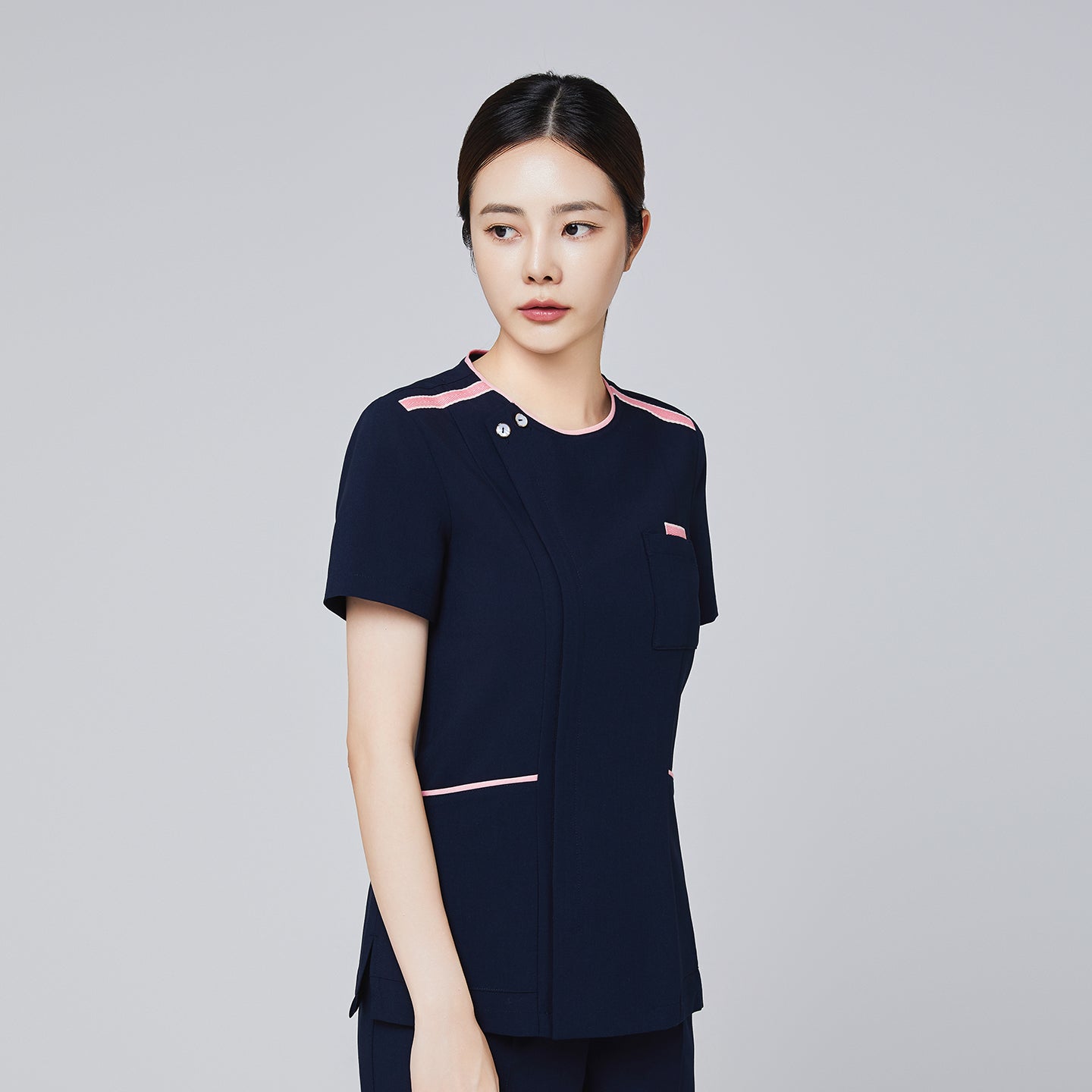 Image of Navy scrub top with pink accents and a modern design, featuring a front pocket and short sleeves, modeled by a woman,Navy