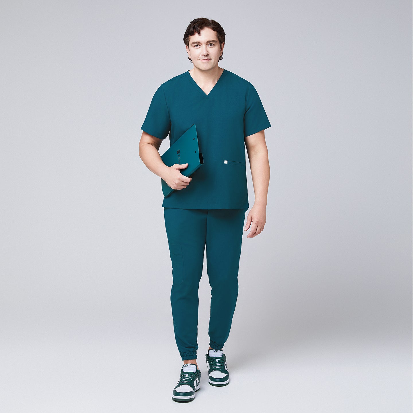 Image of Ocean teal scrub top with two pockets and matching ocean teal jogger scrub pants with a ocean teal binder in hand,Ocean teal