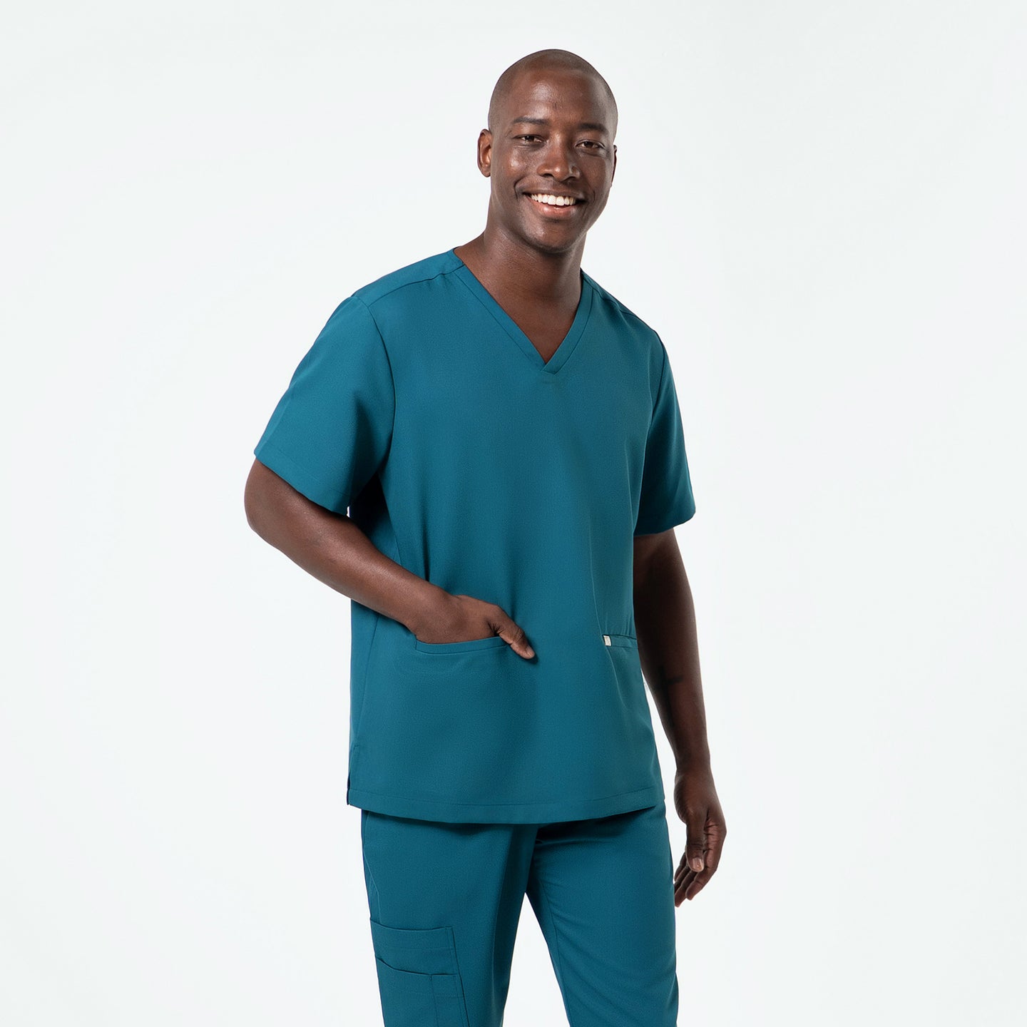 Image of In this front-facing shot, the Smoky-Blue scrub top is shown with its smooth, flexible fabric and minimal double-pocket layout, as the model stands naturally with one hand tucked into the pocket, emphasizing the garment’s comfort and utility for busy medical environments.