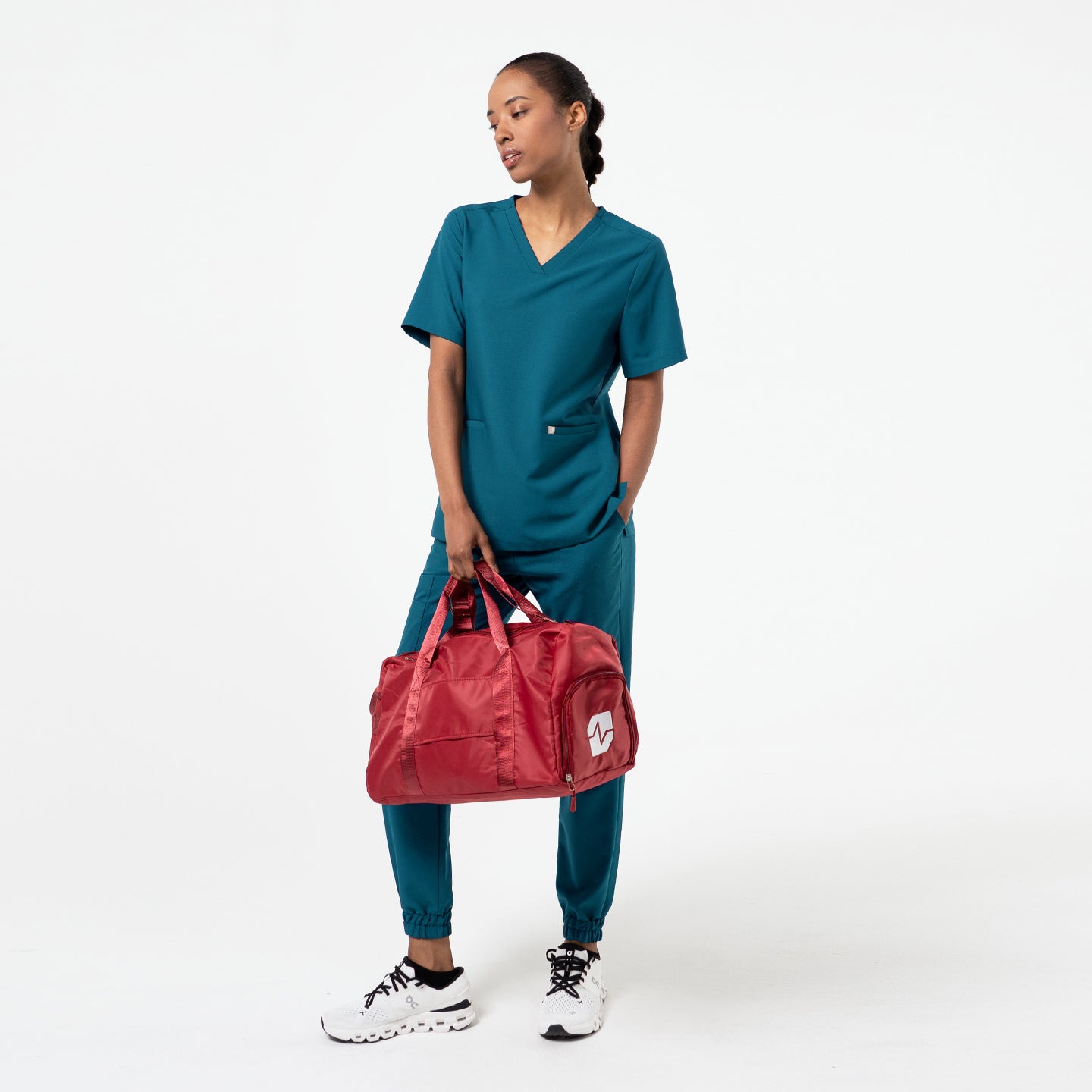 Ocean Teal double-pocket scrub top styled with matching jogger pants, featuring a clean V-neck and roomy pockets while carrying a red duffel bag.