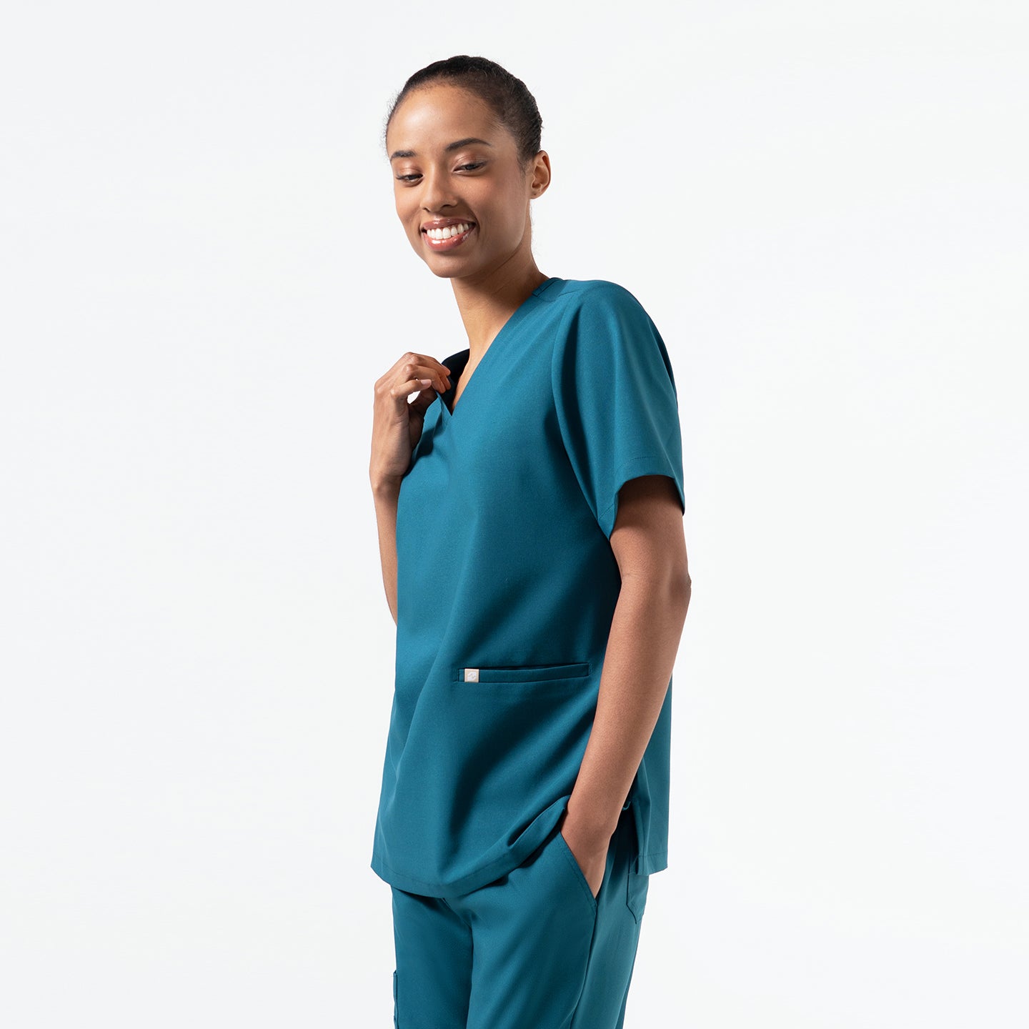Model wearing an Ocean Teal double-pocket scrub top with a relaxed V-neck fit, styled with matching scrub pants for a clean, professional look.