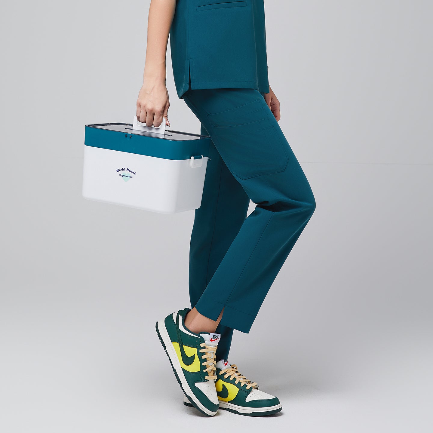 Ocean teal scrub top and ocean teal straight scrub pants with a split hem, with green sneakers and a medical box in hand,Ocean teal