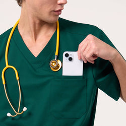 Image of Wearing a Pine Green scrub top, the male model places a smartphone into the chest pocket while a yellow stethoscope hangs around his neck.