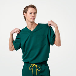 Image of A male model wearing an Eco Hunter Green scrub top and pants, posing with both hands lifting the shirt slightly at the shoulders.