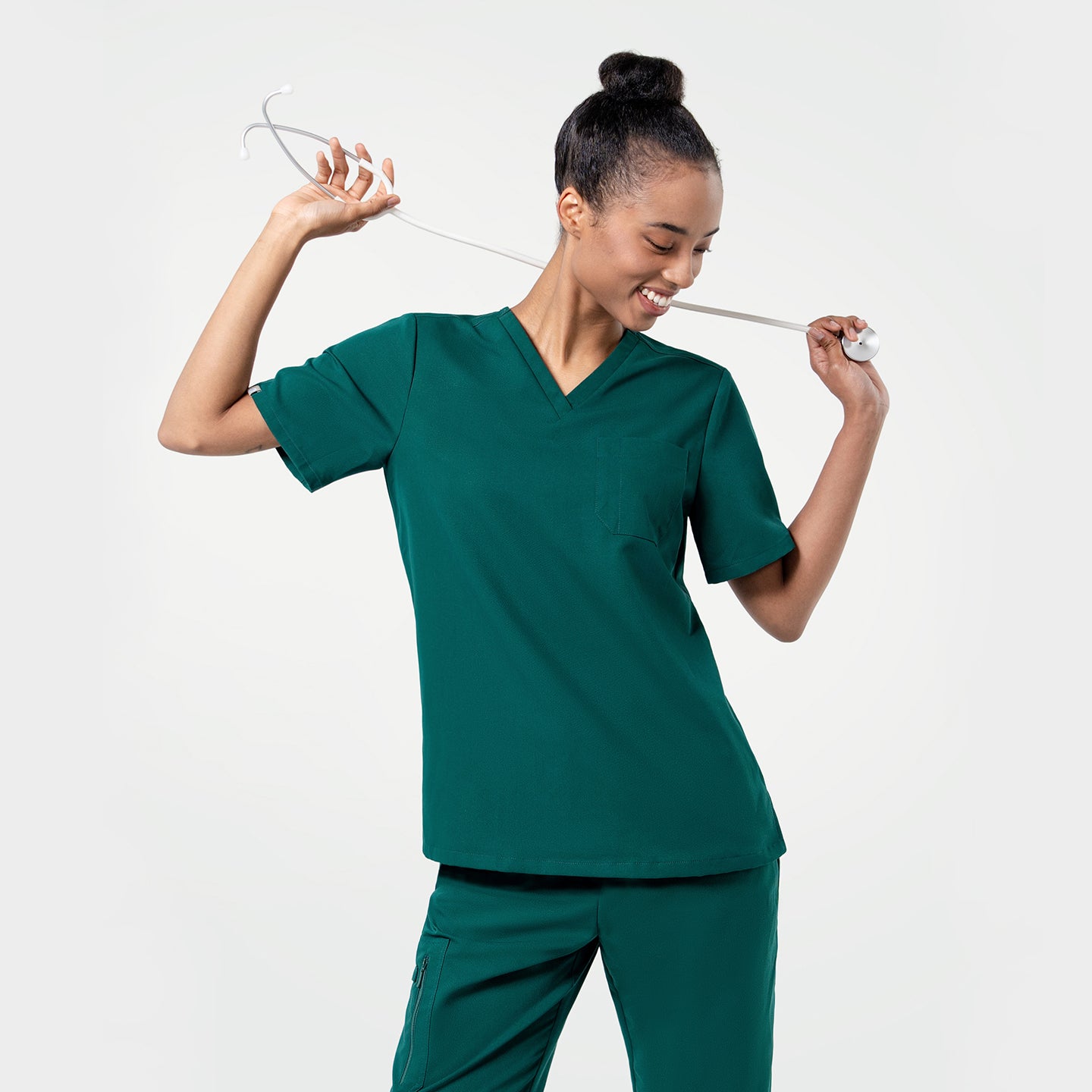 Image of Model in the Women's Pine Green 3-Pocket Scrub Top, posing casually with a white stethoscope, upper body shot