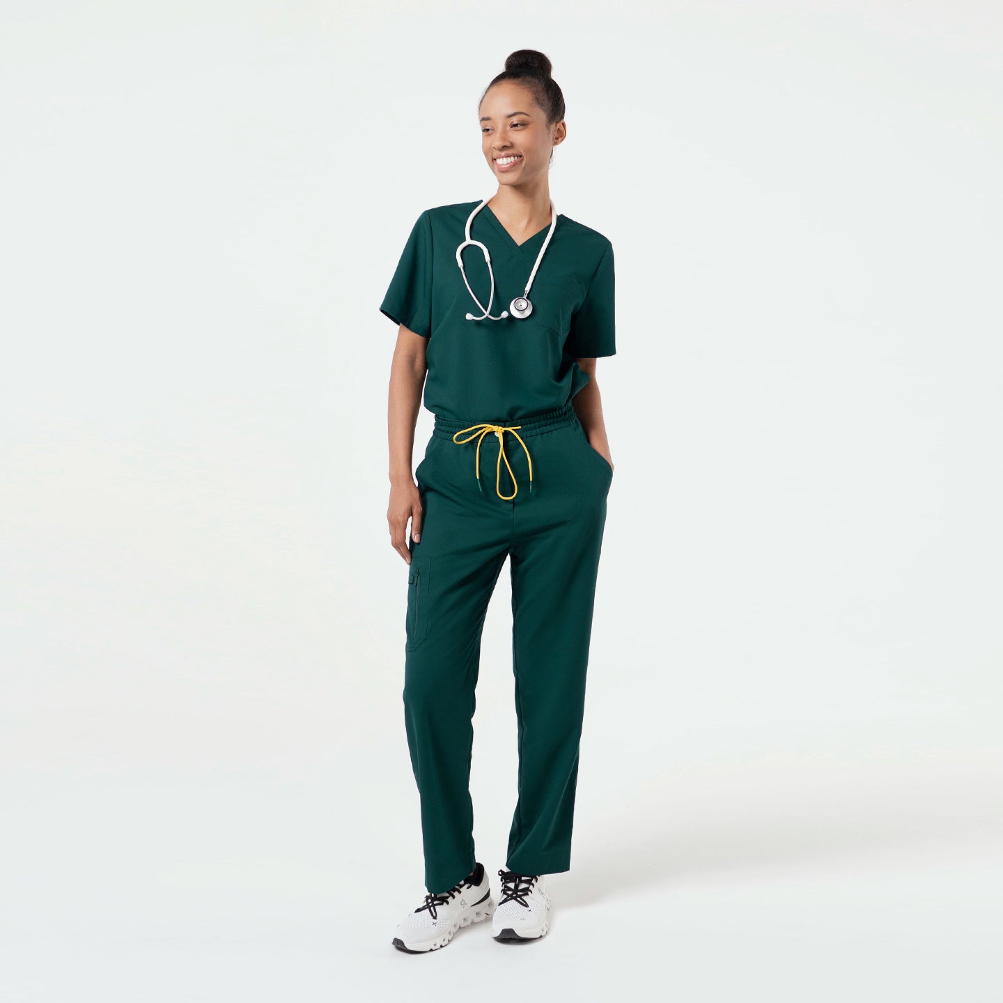 A healthcare professional wearing a Pine Green scrub top with a V-neck and single chest pocket, styled with matching pants and a stethoscope.