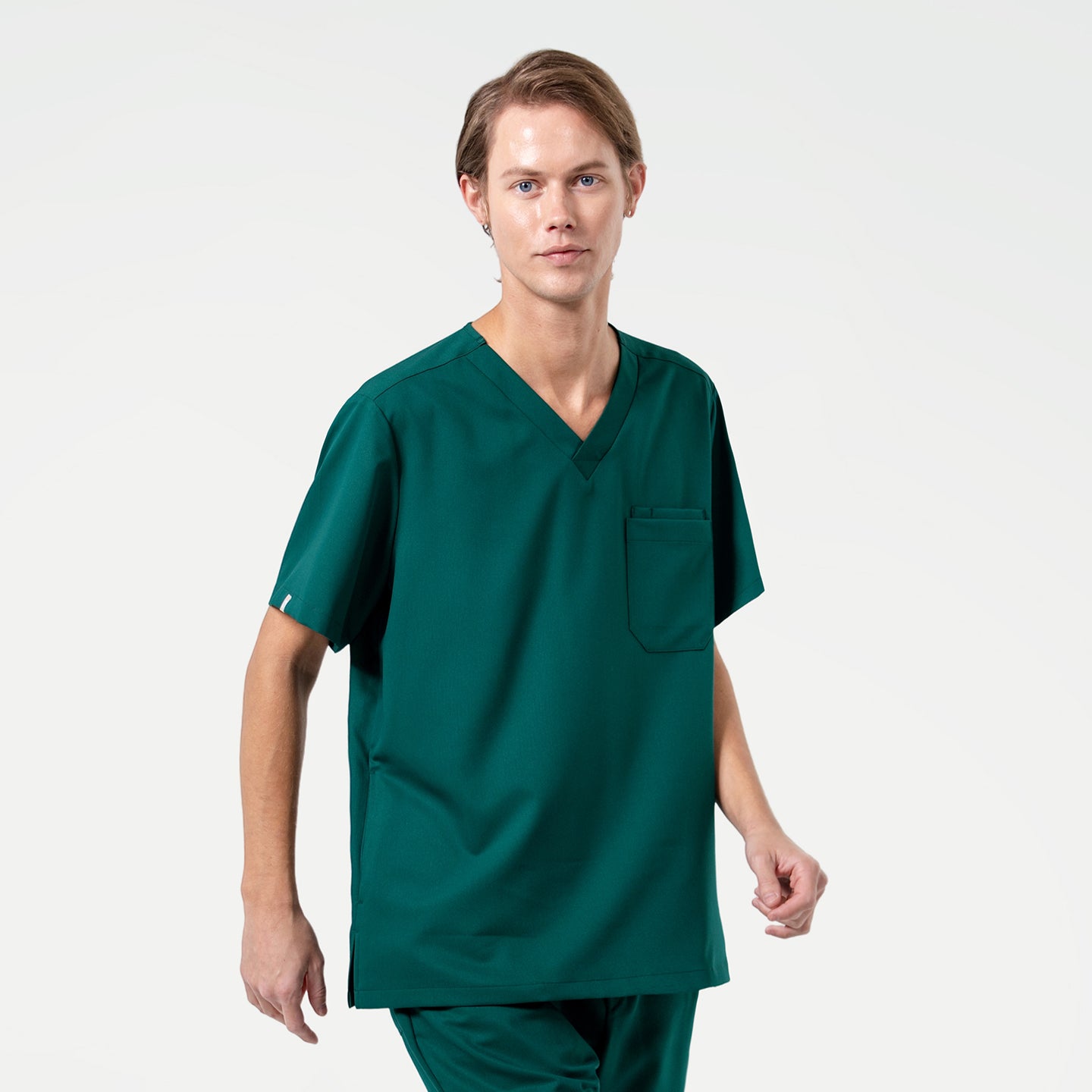 Wearing a Pine Green scrub set, the male model stands upright and faces forward with a calm, neutral expression, his arms relaxed at his sides, showcasing the clean and professional look of the outfit.
