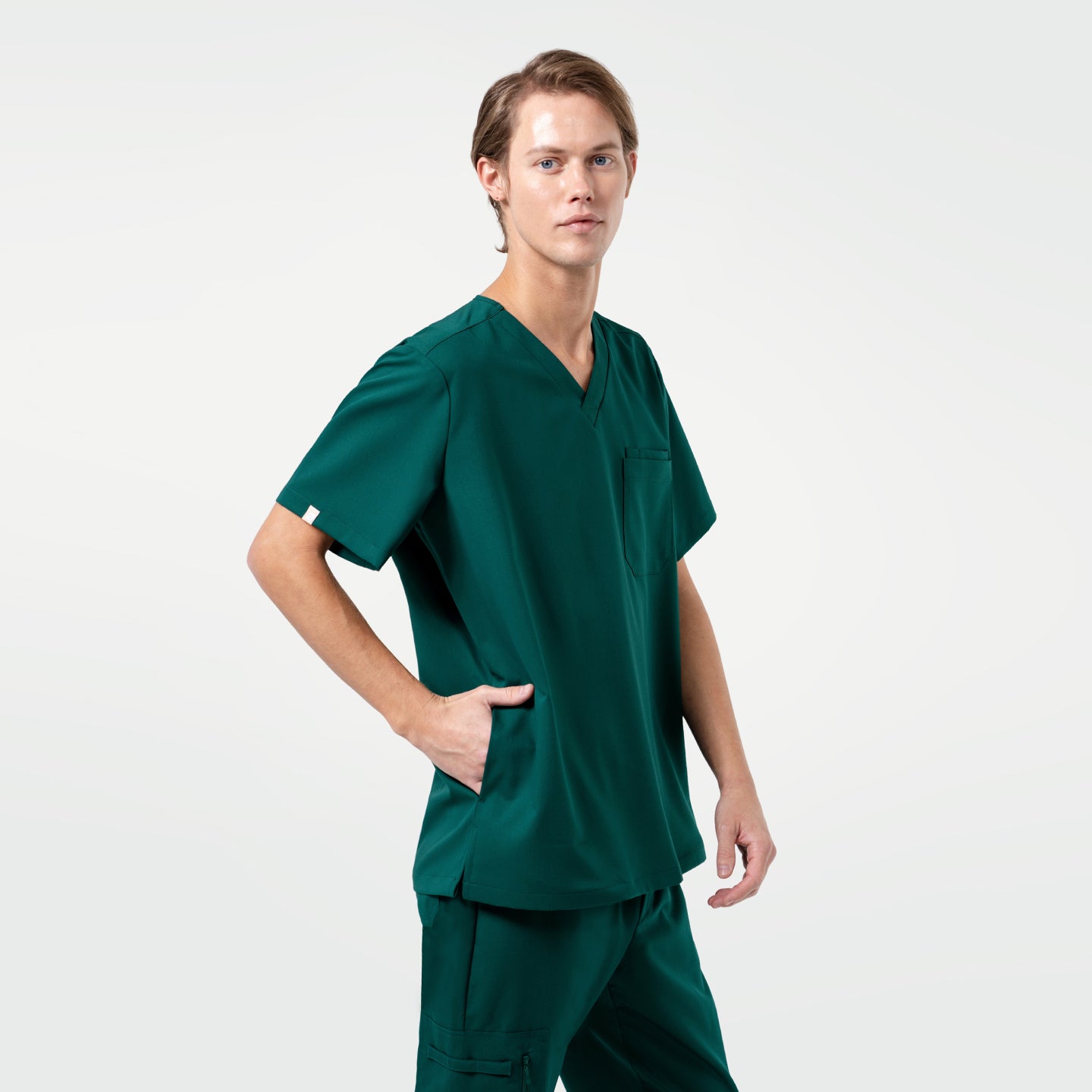 Image of A male model wears the Zenir Pine-Green 3-Pocket Scrub Top with matching pants, showing a clean V-neck design, a functional chest pocket, and a comfortable fit that allows easy movement.