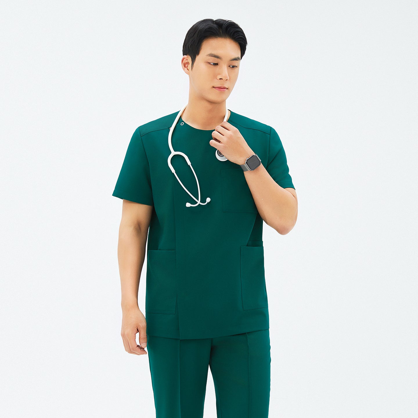 Model adjusting stethoscope while wearing TUL DS-191 Men's Round Snap Zipper Scrub Top in Pine Green, featuring front pockets and short sleeves.