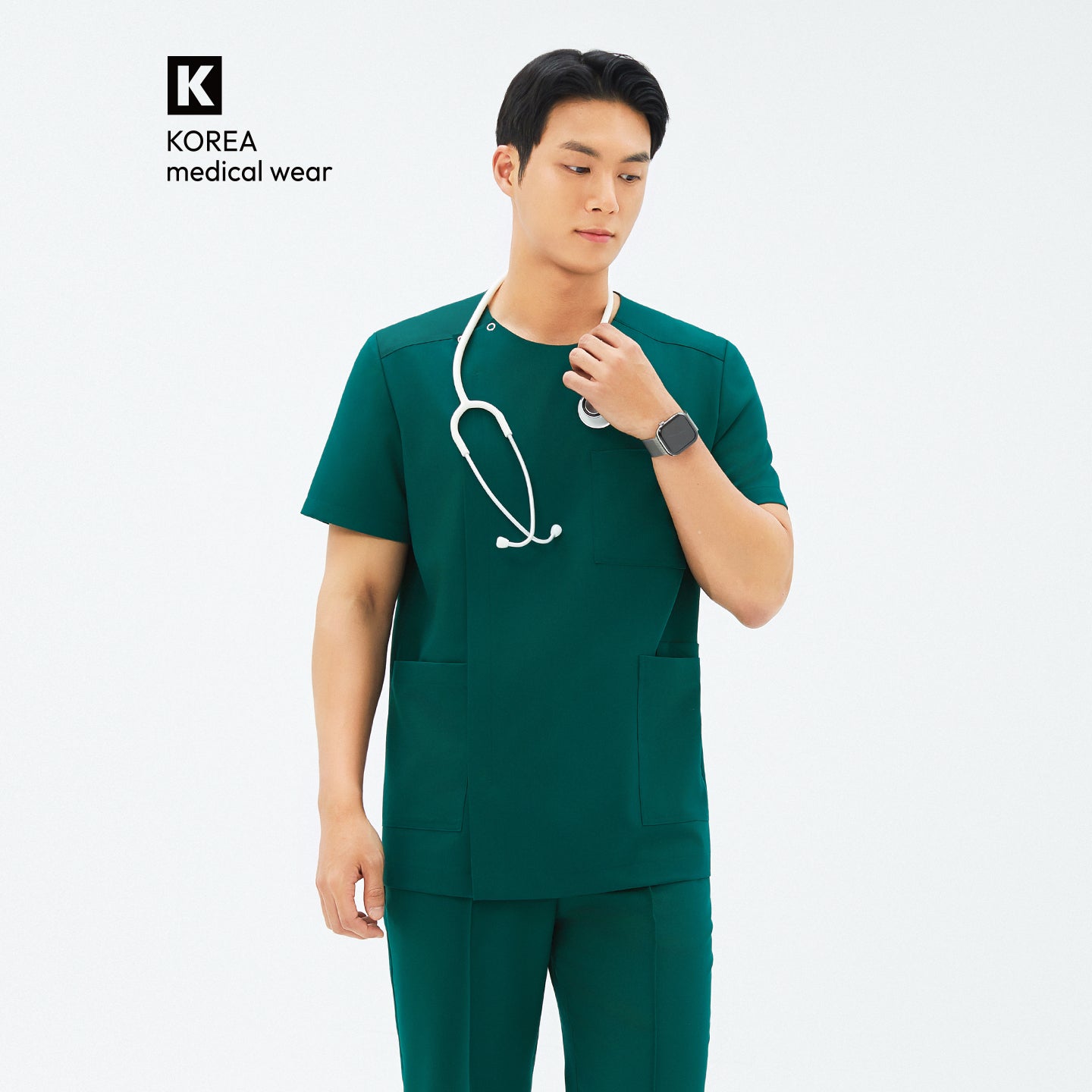 Image of Model adjusting stethoscope while wearing TUL DS-191 Men's Round Snap Zipper Scrub Top in Pine Green, featuring front pockets and short sleeves.