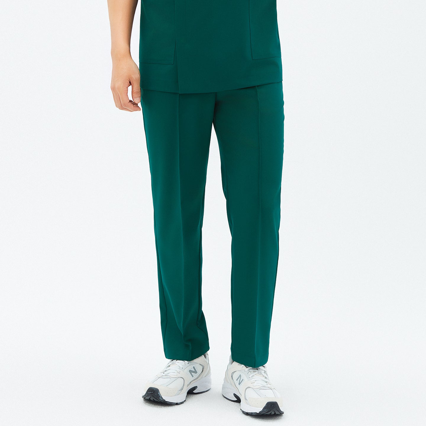 Image of Close-up front view of TUL Men’s Premium Banding Pants in Pine Green, showing the straight-leg cut and matching scrub top hem. The model’s white sneakers are visible at the bottom.