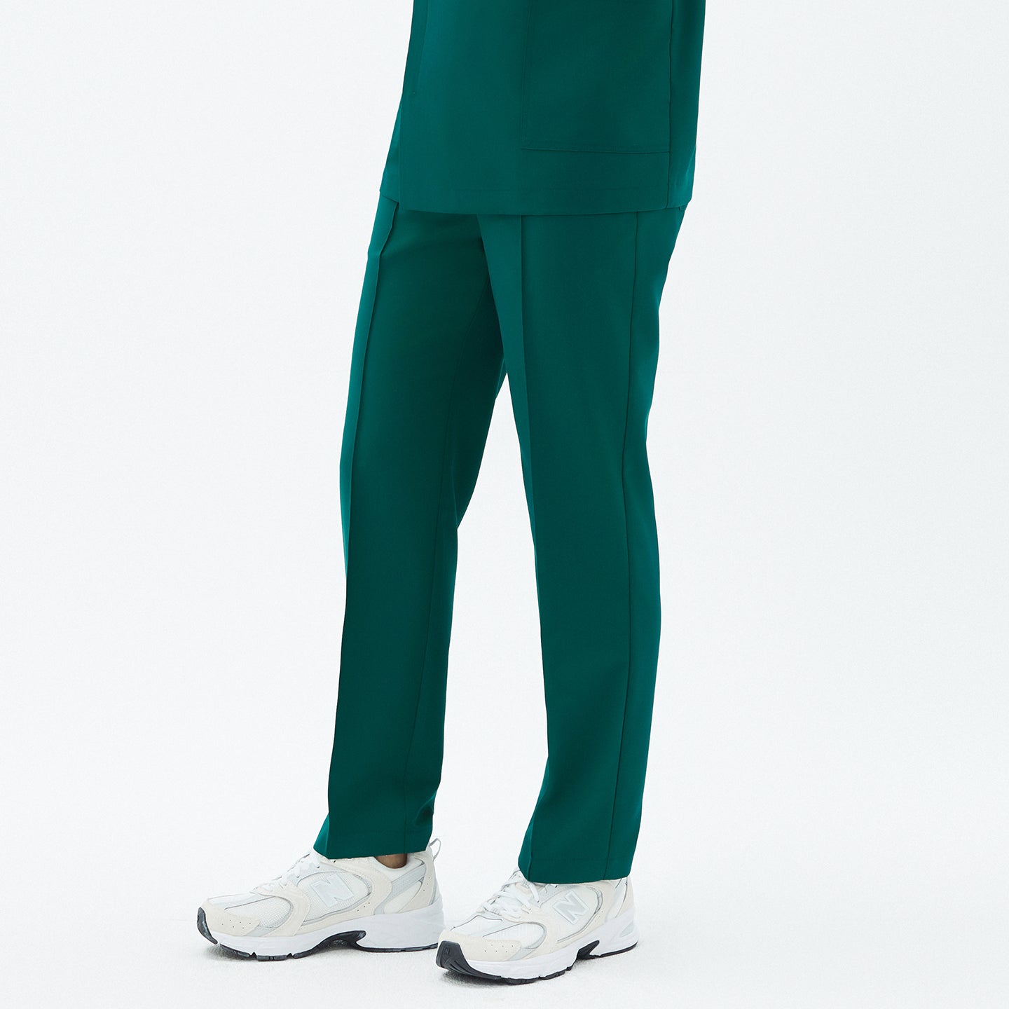 Image of Side angle of TUL Men’s Premium Banding Pants in Pine Green, emphasizing the crisp front seam and discreet waistband. The model’s scrub top aligns neatly at the waist, and white sneakers complete the outfit.