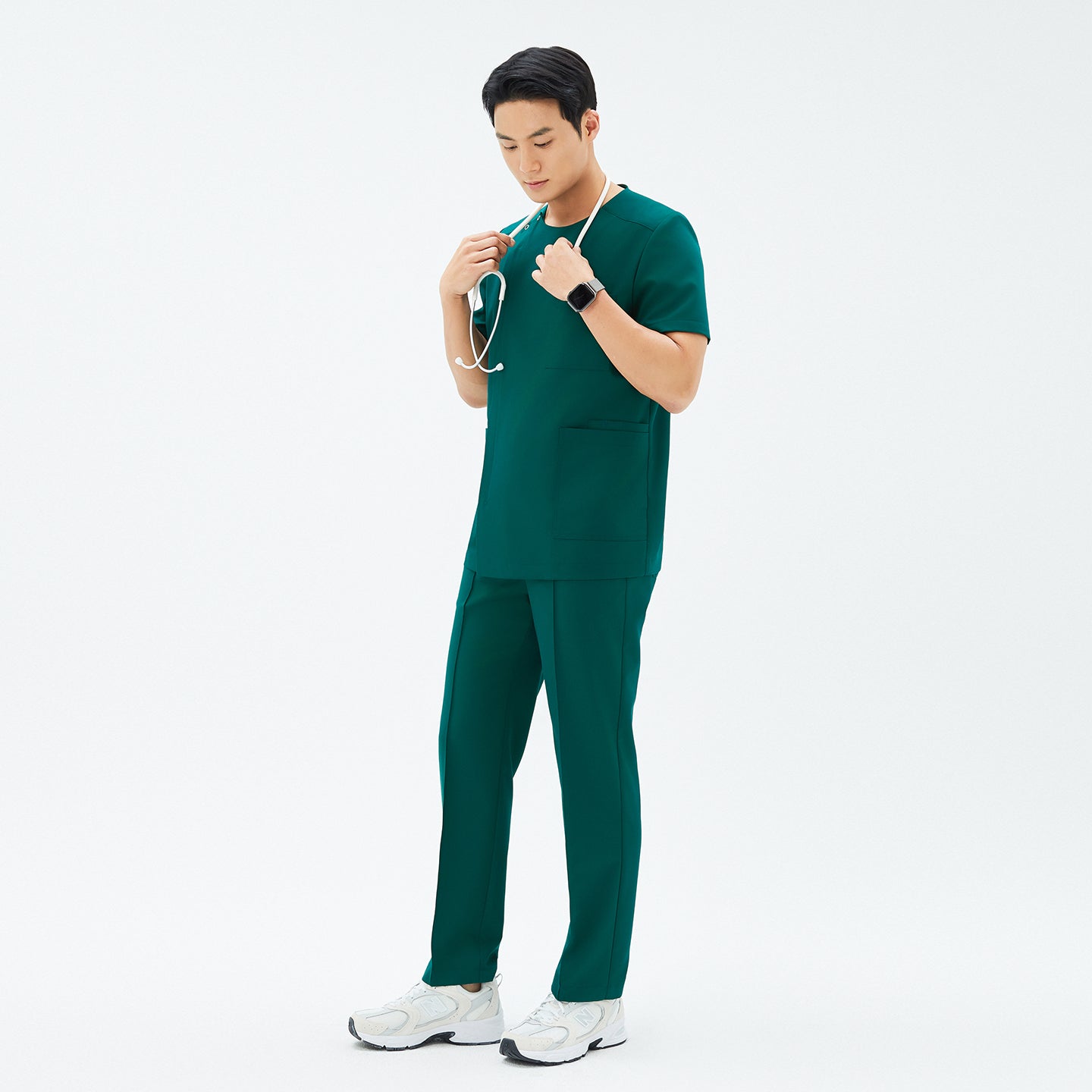 Image of Male model wearing TUL Men’s Premium Banding Pants in Pine Green, standing in a relaxed pose with a stethoscope around his neck. The pants feature polished seams, and the matching scrub top creates a unified professional look.