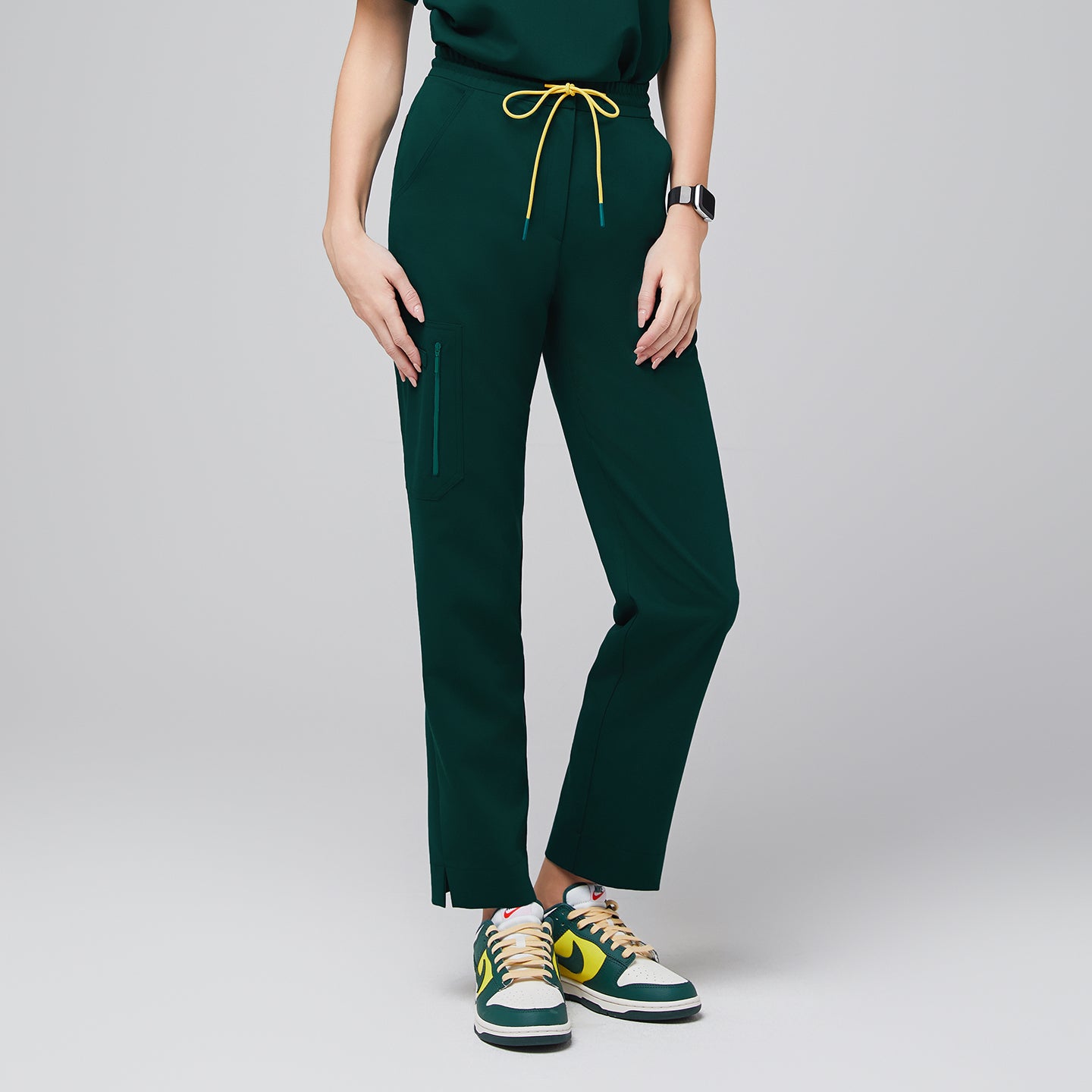 Image of Scrub pants with a drawstring waist, zipper pocket, and split hem, paired with sporty sneakers for a functional and professional style,Pine Green