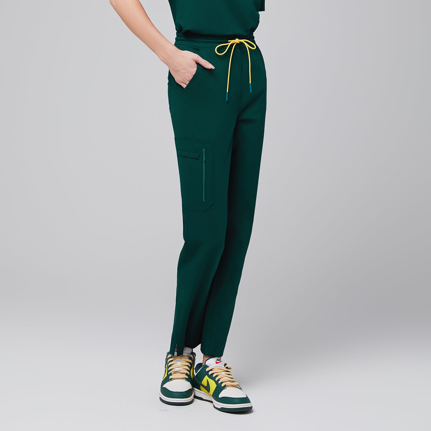 Image of Drawstring scrub pants with a zipper pocket and split hem, styled with casual sneakers for a functional and modern professional outfit,Pine Green