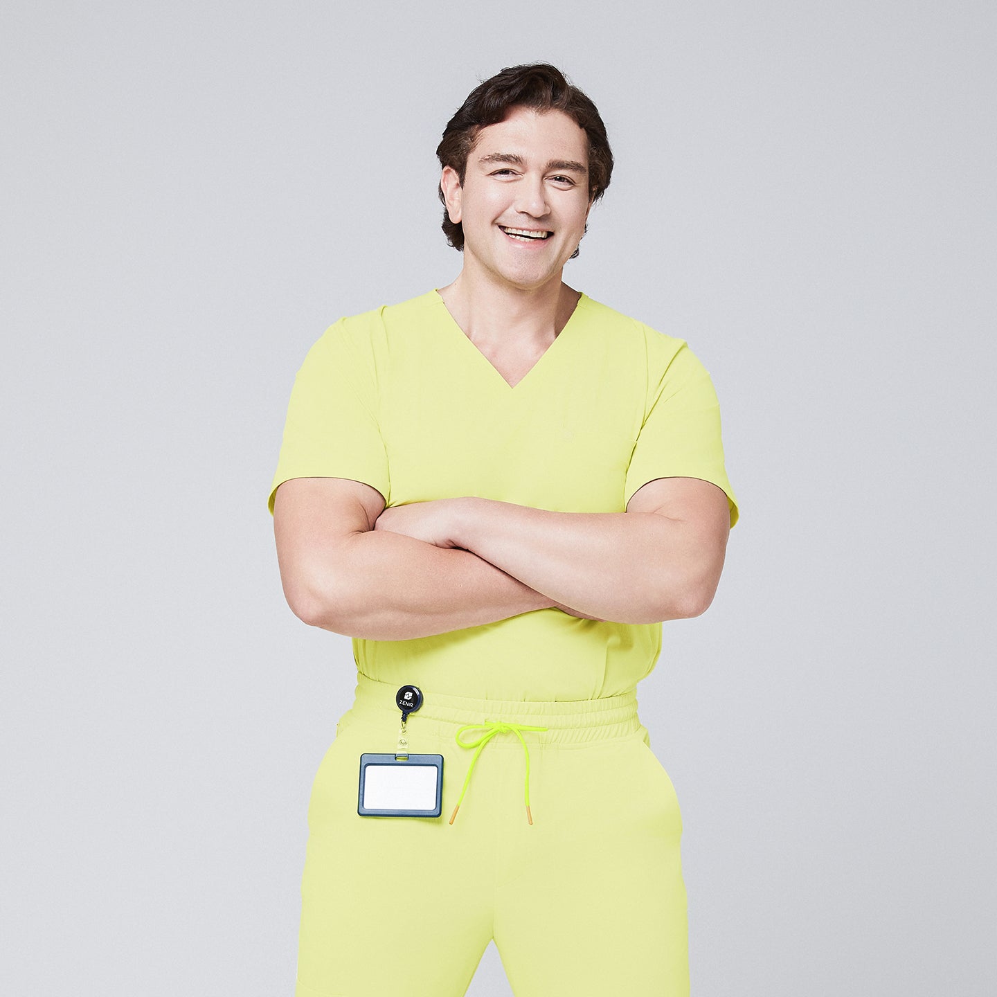 Image of Male model wearing a pineapple yellow V-neck single-pocket scrub top with matching pants and a badge holder, smiling with arms crossed,Pineapple Yellow