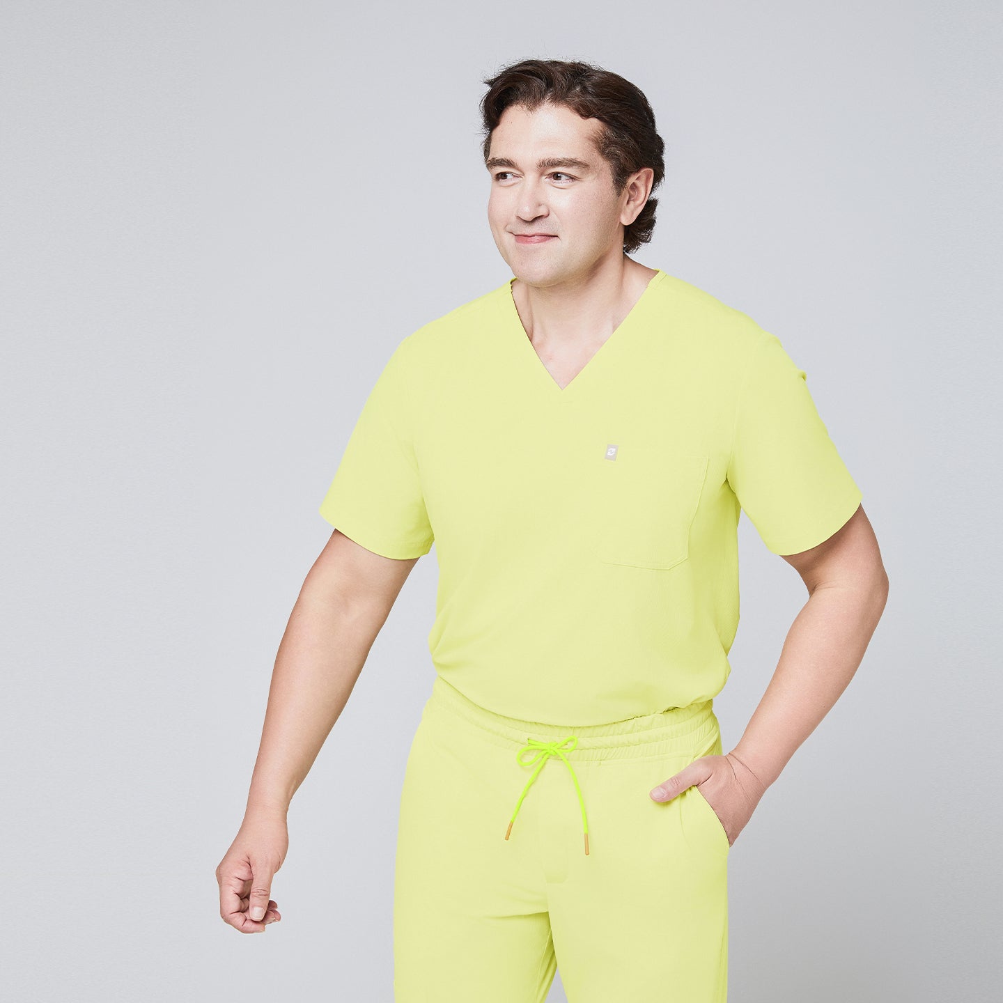 Image of Male model wearing a pineapple yellow V-neck single-pocket scrub top with matching drawstring pants, smiling,Pineapple Yellow