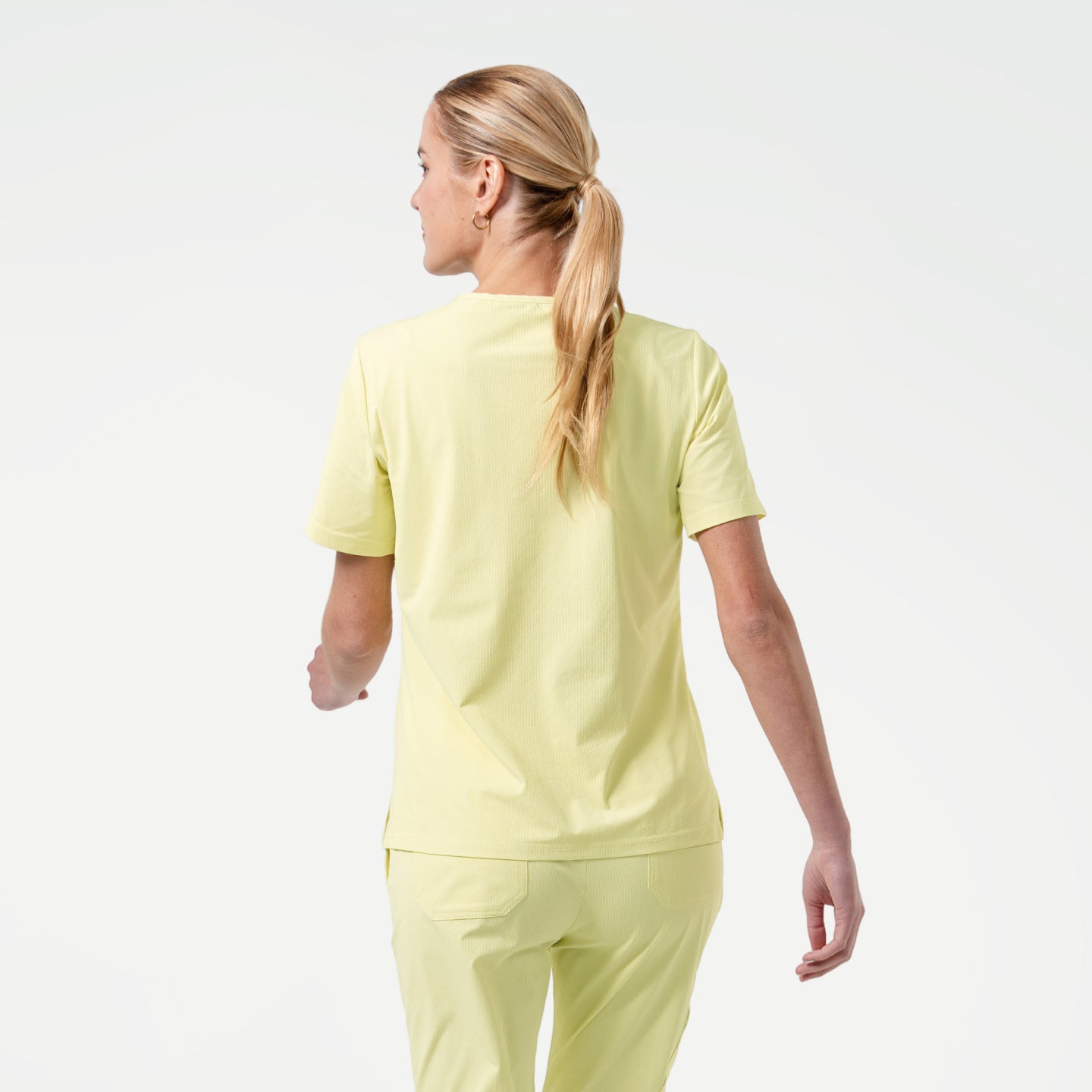 Back view of Pineapple Yellow scrub top with short sleeves, paired with matching scrub pants, shown against a light background.
