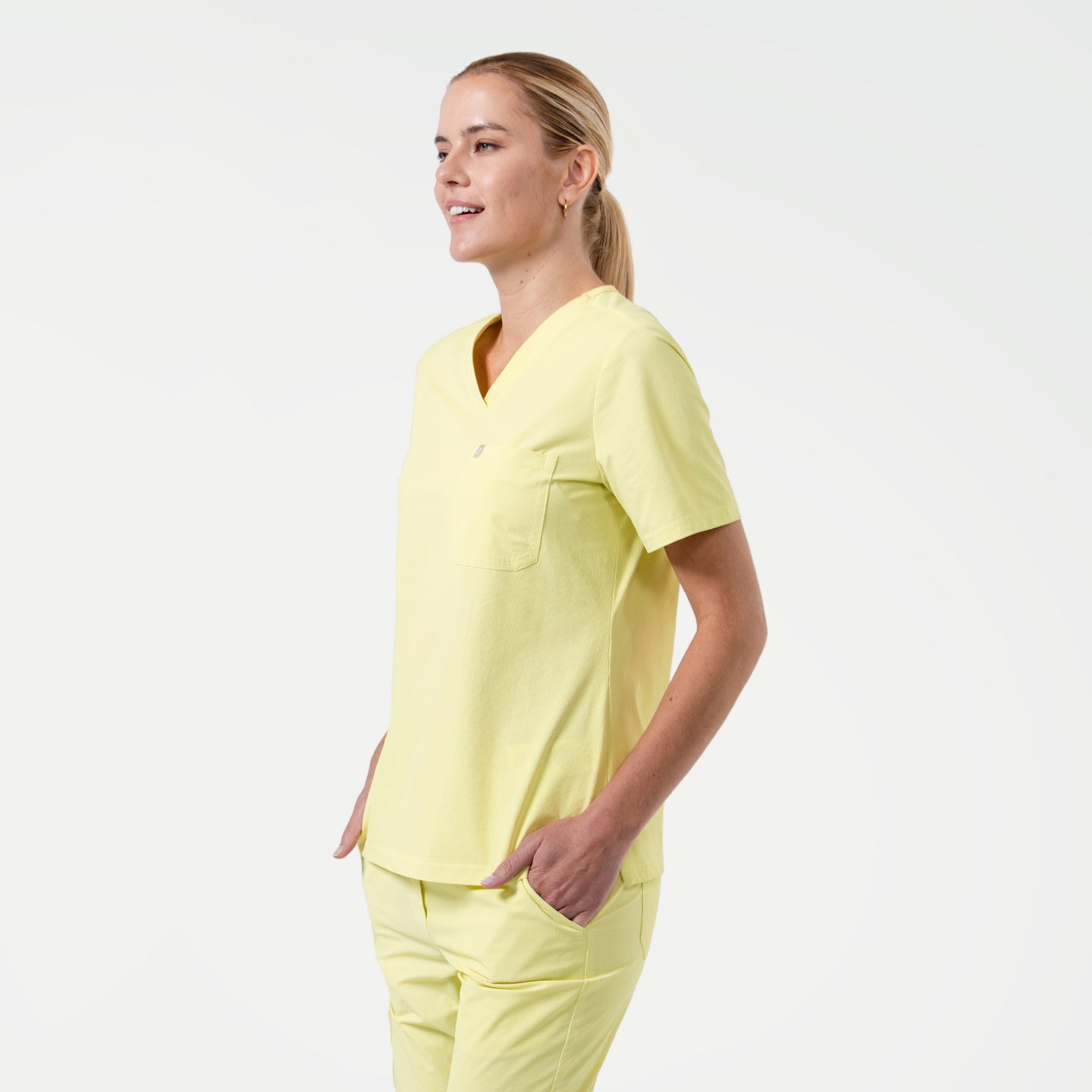 Pineapple-Yellow Zenir scrub top with a single chest pocket, captured in a relaxed side pose that emphasizes its breathable texture, short sleeves, and coordinated scrub set.
