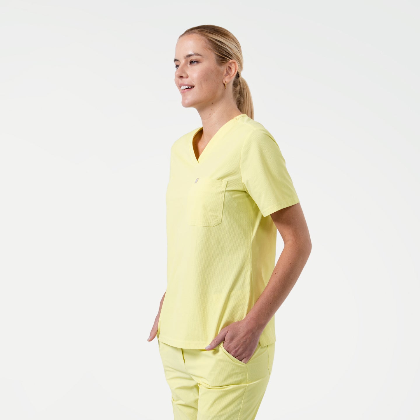 Model in Pineapple Yellow single pocket scrub top with short sleeves and chest pocket, paired with matching scrub pants.
