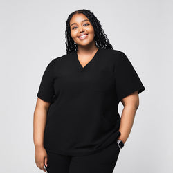 Image of Smiling female medical professional wearing a black scrub top with a single chest pocket, standing with her hand in her pocket,Rich Black