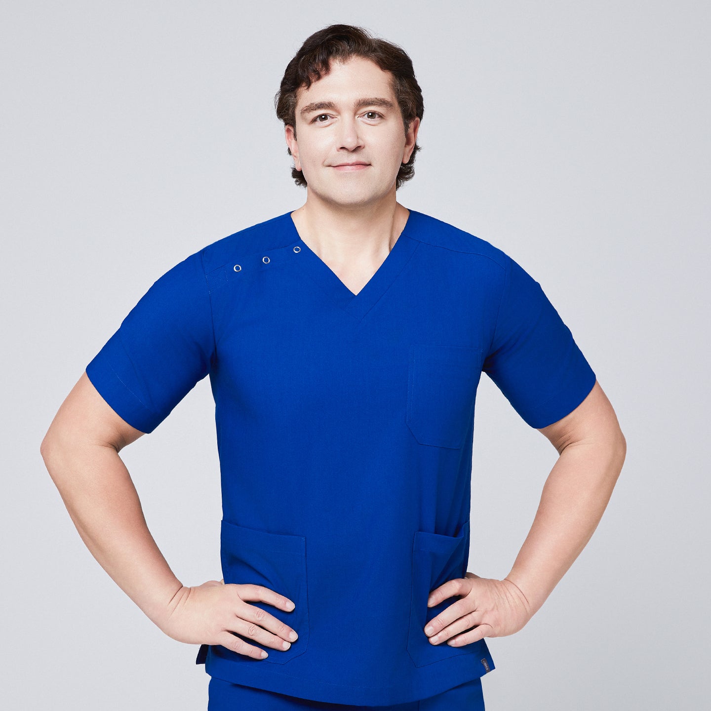 Image of Man wearing Zenir royal blue 3-button scrub top with chest and lower pockets, posing with hands on hips,Royal Blue