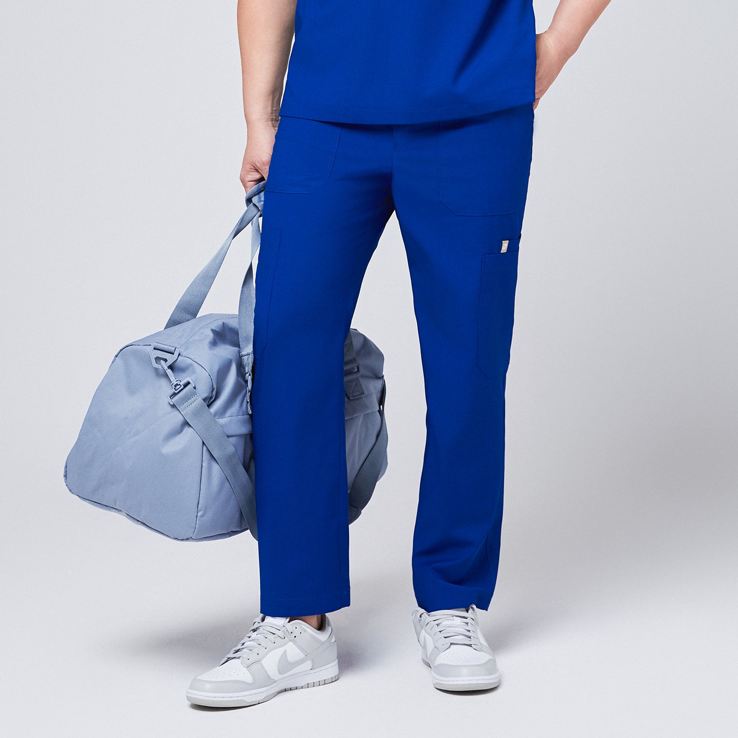Image of Close-up of royal blue 8-pocket scrub pants paired with a matching scrub top, white sneakers, and a light blue duffle bag,Royal Blue