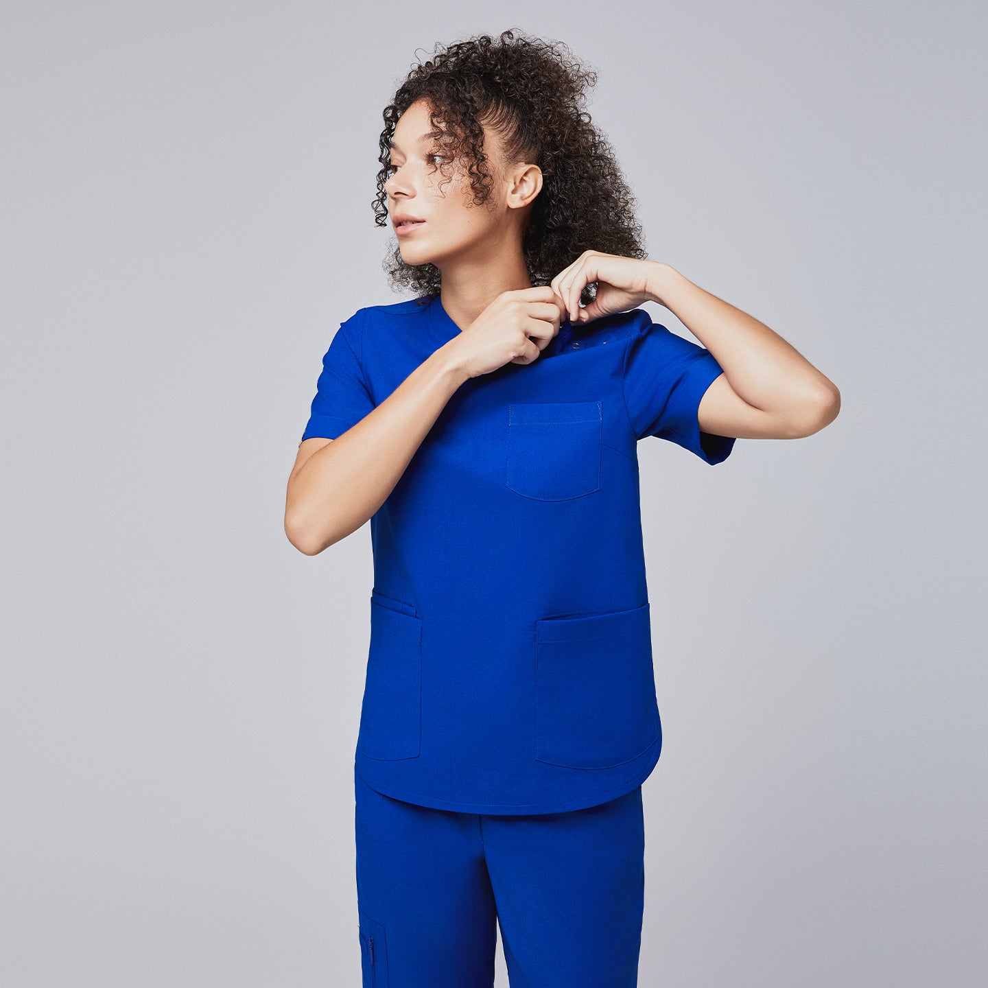 A woman adjusting the button closure on the shoulder of a royal blue scrub top, highlighting its functional design,Royal Blue