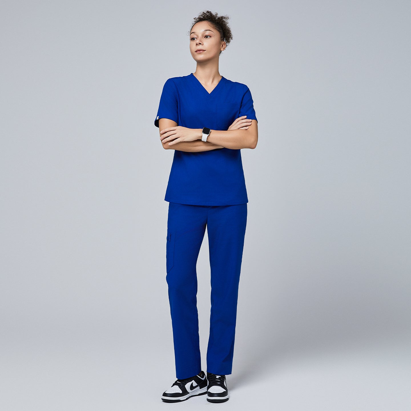 Image of Model wearing a royal blue V-neck scrub set featuring a short-sleeve top and split-hem pants with zipper pockets, paired with black sneakers for a sleek and professional look,Royal Blue