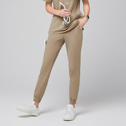Image of Female wearing sand beige jogger scrub pants with side pockets, holding a stethoscope, paired with white sneakers,Sand Beige