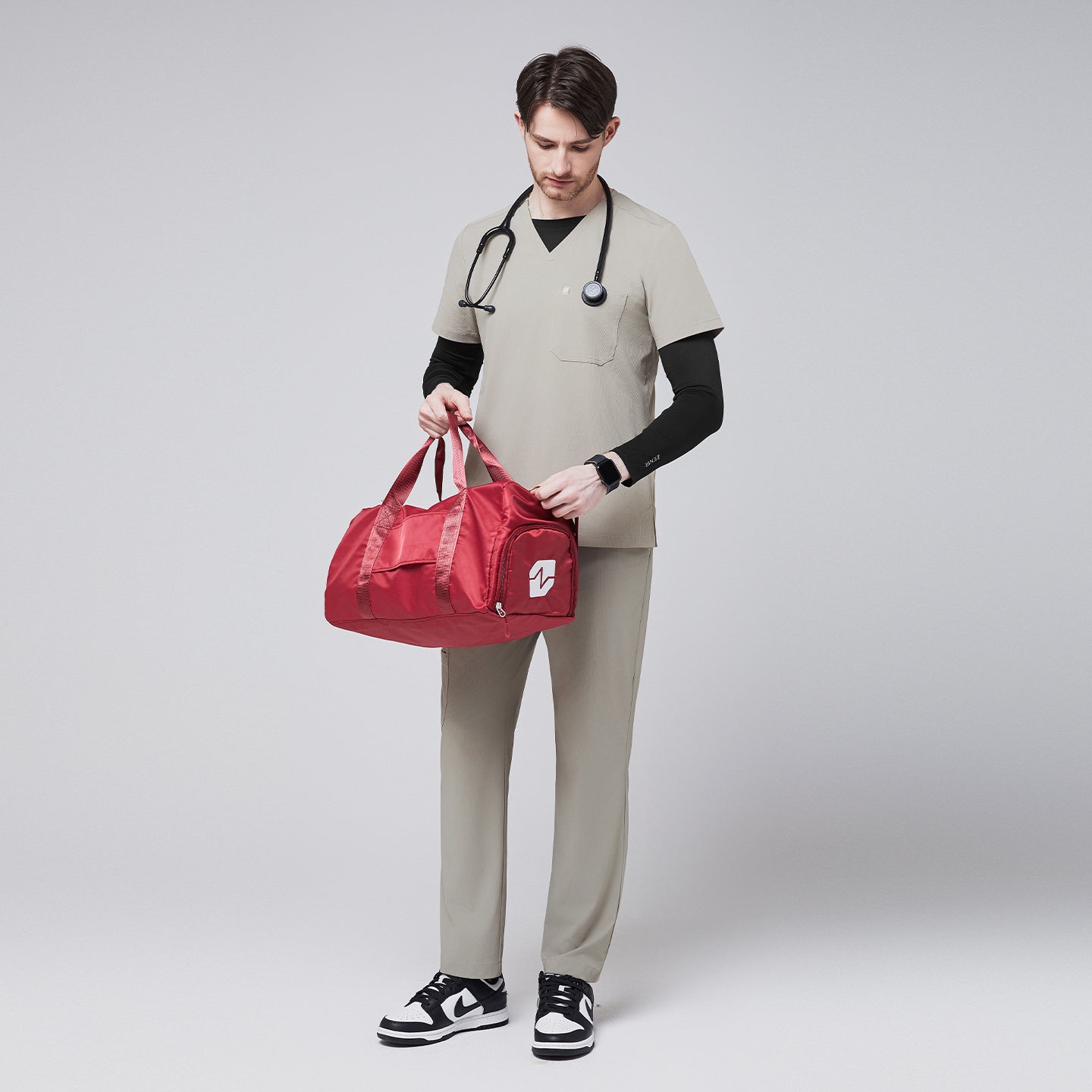 Image of Man wearing sand khaki scrub pants and a matching V-neck top with a black undershirt, holding a red medical duffel bag and a stethoscope, paired with black-and-white sneakers,Sand Khaki