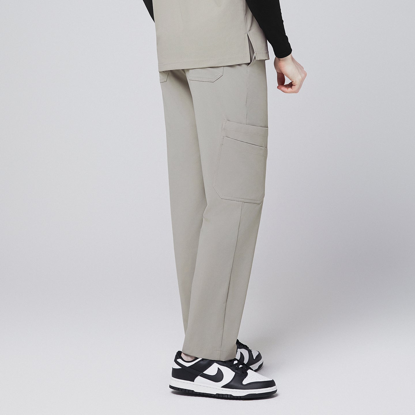 Image of Side view of sand khaki scrub pants with a functional side pocket and back pockets, paired with black-and-white sneakers,Sand Khaki