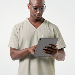 Image of The male model is dressed in Sand Khaki scrubs, wearing glasses while holding and reviewing a tablet, creating a professional and focused look.
