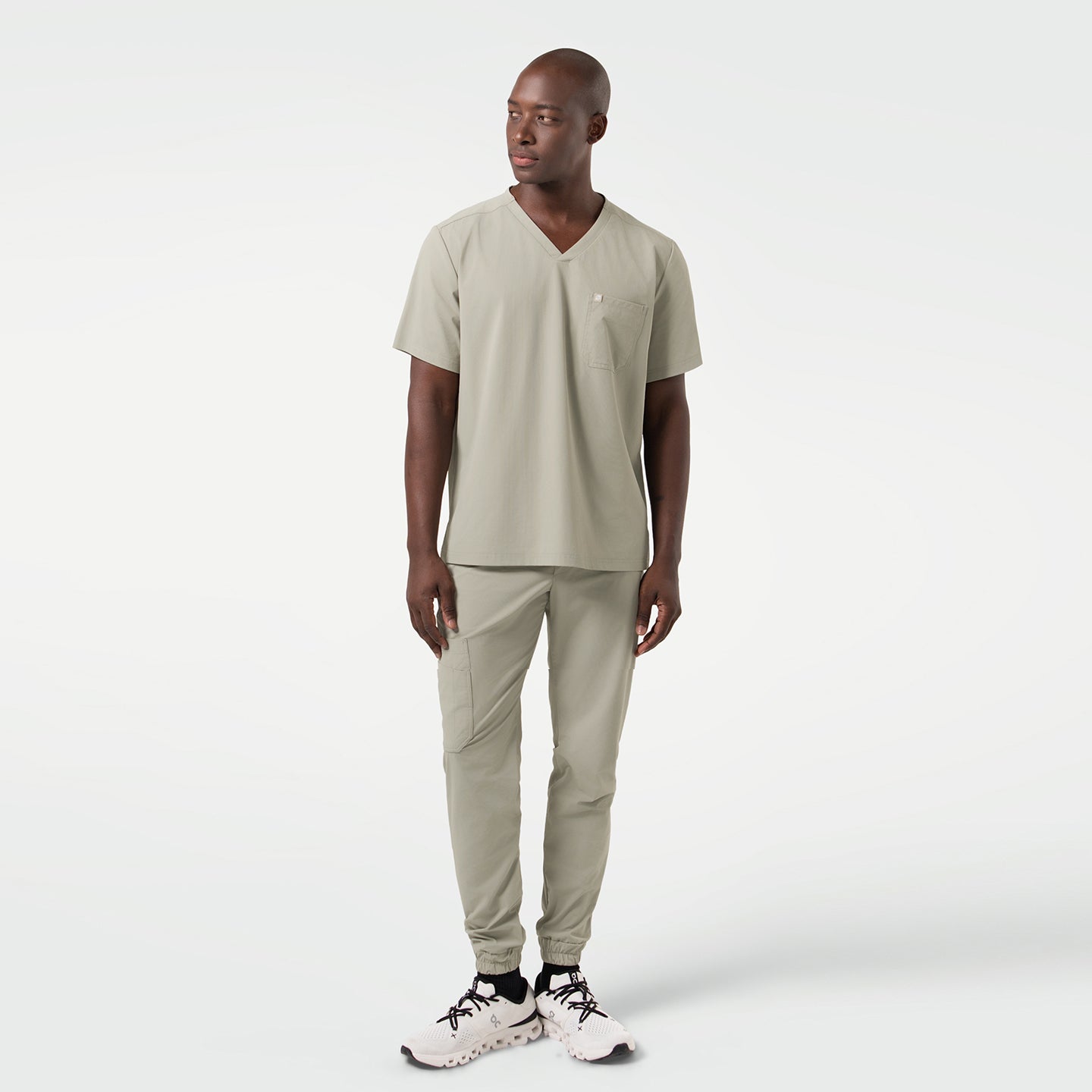 The male model is seen in a full-body shot dressed in Sand Khaki scrubs, standing with a relaxed posture and his gaze directed slightly to the side, showcasing the streamlined fit and contemporary style of the set.