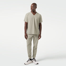 Image of The male model is seen in a full-body shot dressed in Sand Khaki scrubs, standing with a relaxed posture and his gaze directed slightly to the side, showcasing the streamlined fit and contemporary style of the set.