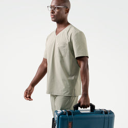 Image of The male model in Sand Khaki scrubs walks confidently while carrying a sturdy blue equipment case, complemented by glasses for a polished, professional appearance.