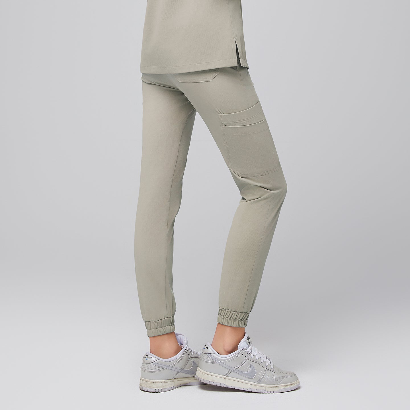 Image of Back view of sand khaki jogger scrub pants showcasing a tailored fit with back pockets and elasticized cuffs, paired with sleek silver sneakers for a modern and professional appearance, Sand Khaki