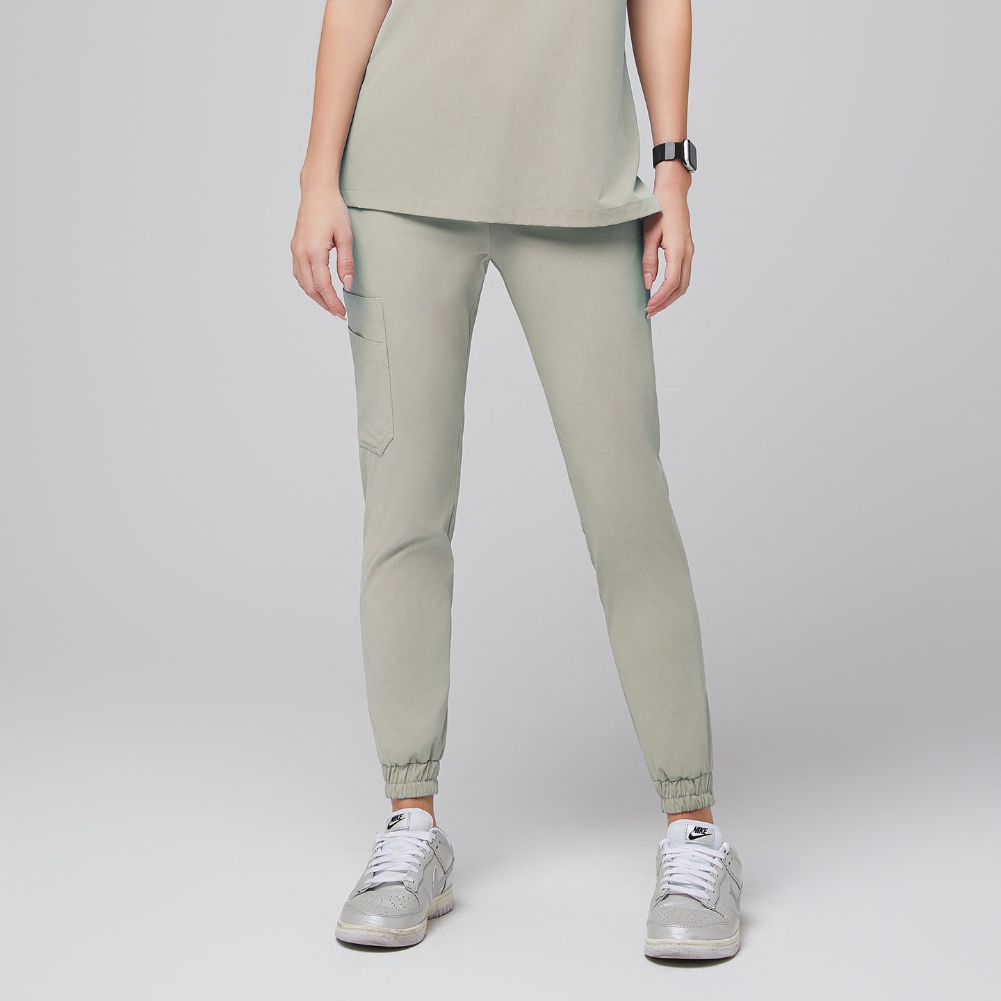 Image of Front view of sand khaki jogger scrub pants featuring an elastic waistband, a side pocket, and cuffed hems, paired with silver sneakers for a stylish and functional look,Sand Khaki