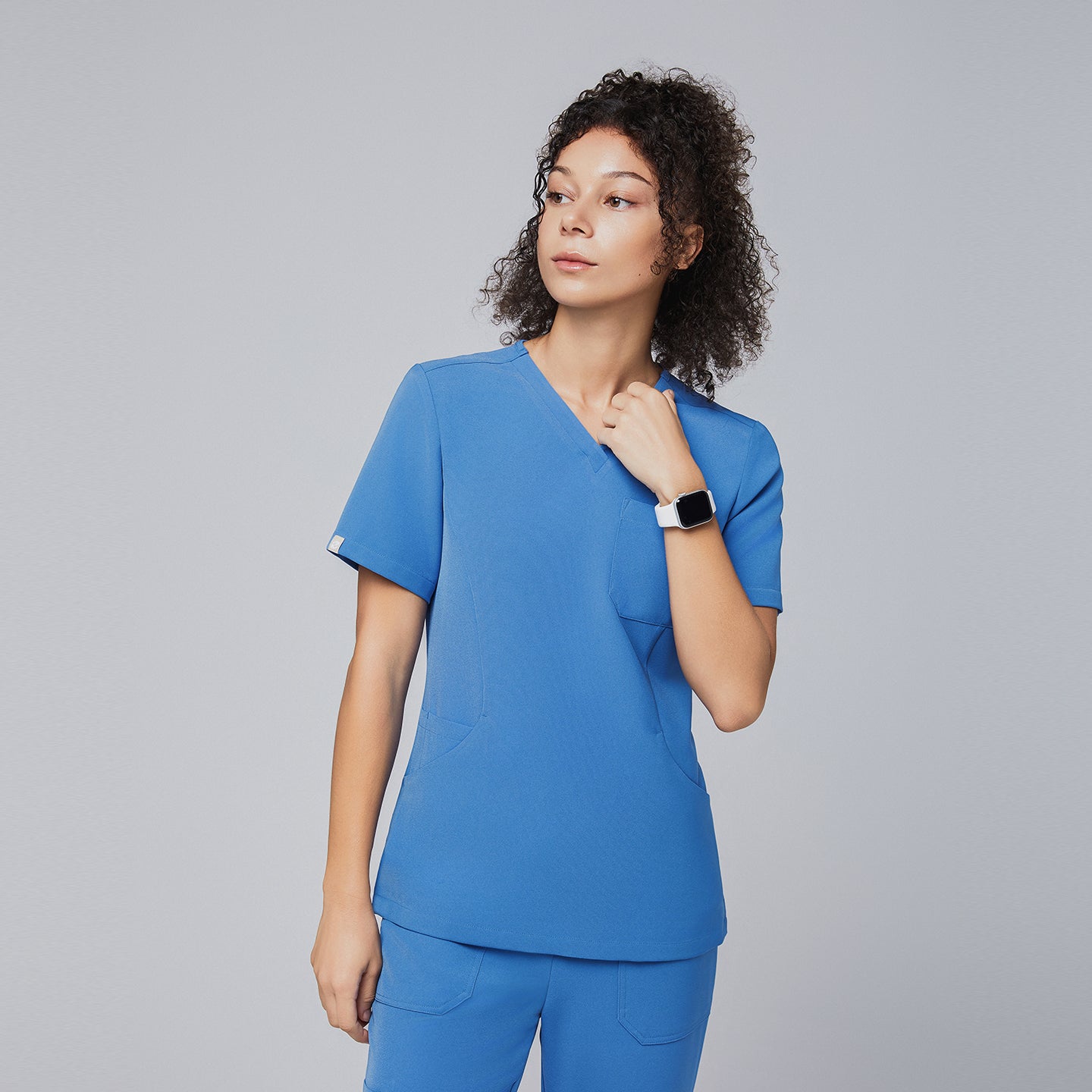 Image of Woman wearing a sky-blue V-neck scrub top with short sleeves and matching pants, looking confidently to the side while showcasing the sleek and professional design of the uniform,Sky Blue
