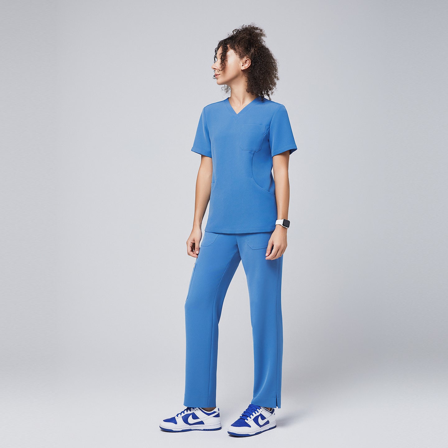 Image of Side view of a woman wearing a sky-blue V-neck scrub top paired with matching straight-leg pants and blue sneakers, exuding a casual yet professional healthcare uniform style,Sky Blue