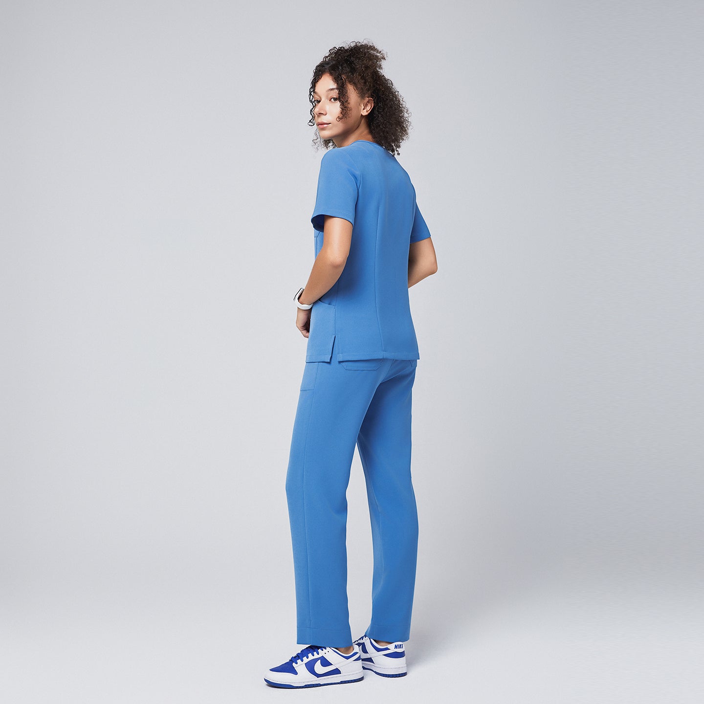 Woman wearing a sky-blue scrub set, viewed from the back and side angle, showcasing the tailored fit and rear design details of the uniform,Sky Blue