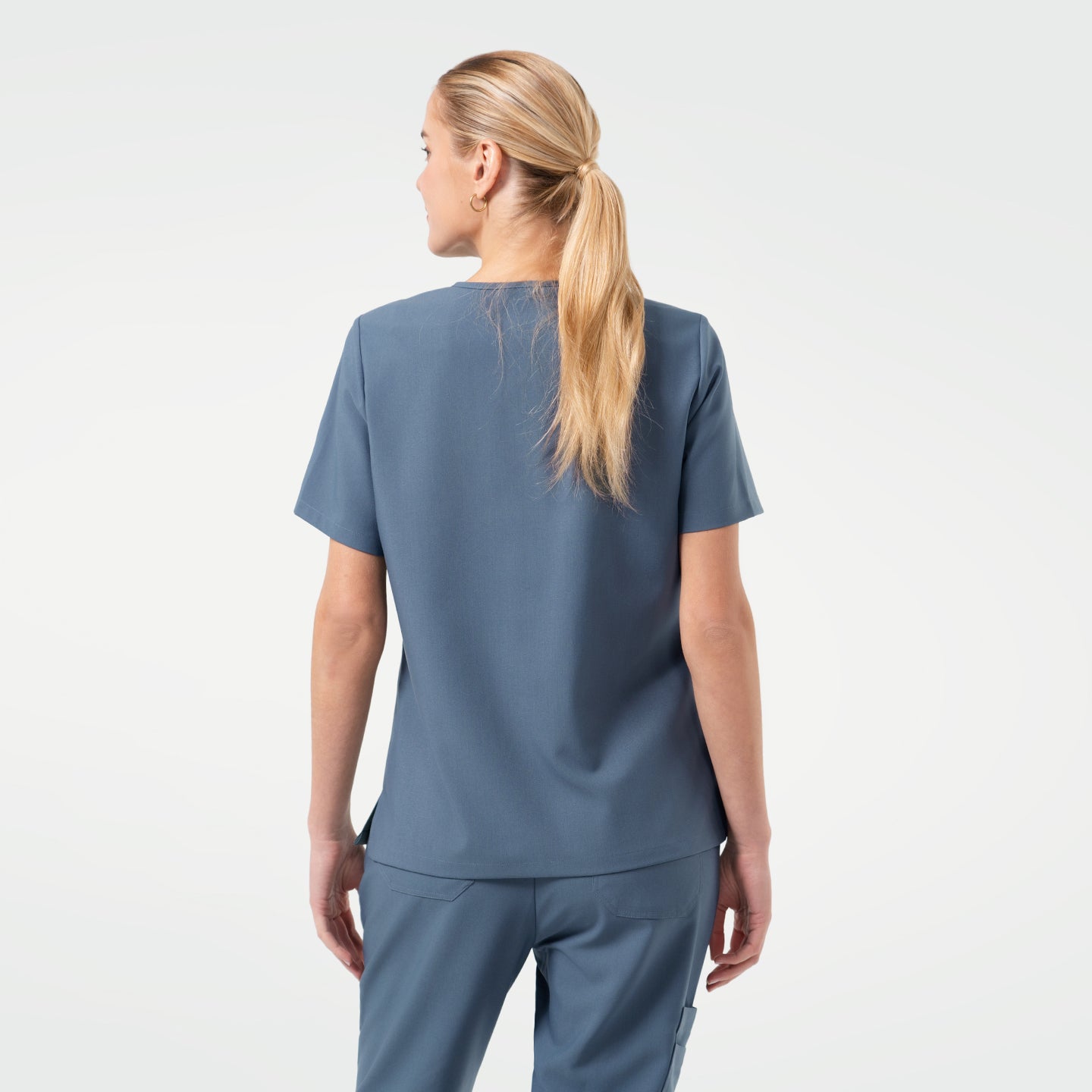 Image of Model is shown from the back, wearing a Smoky Blue scrub top paired with matching scrub pants. 