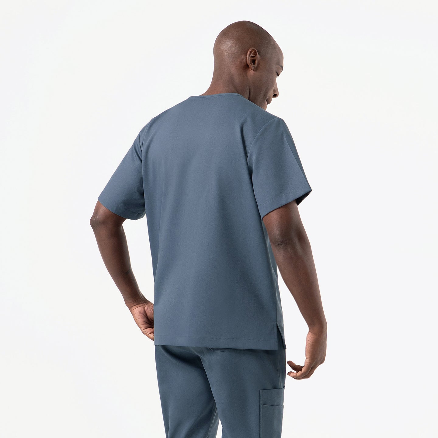 Image of Designed for practicality and effortless wear, the Smoky-Blue double-pocket scrub top is displayed from a back-angle view, emphasizing its straight hem, relaxed structure, and durable fabric that pairs neatly with matching cargo scrub pants.