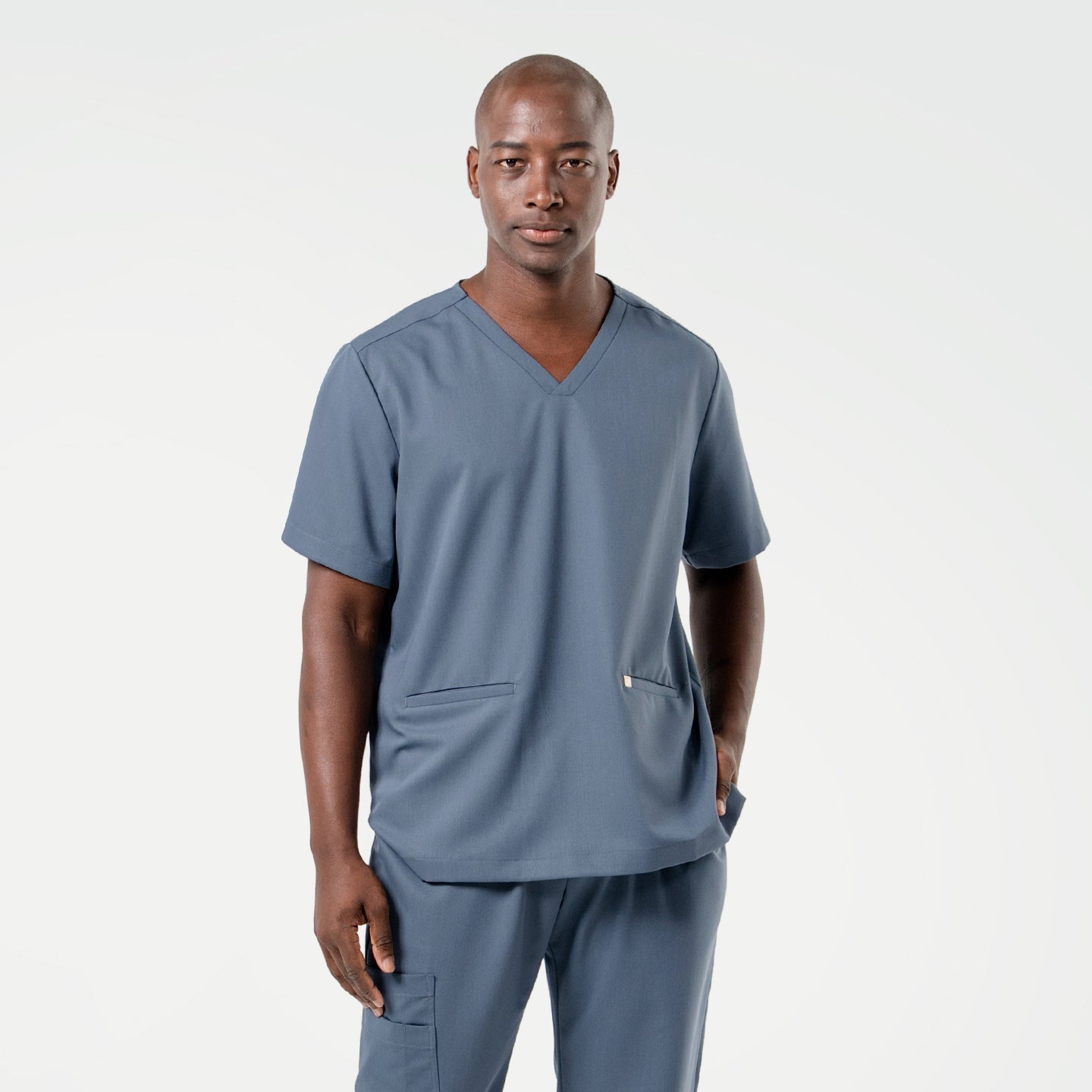 Image of Wearing a Smoky Blue scrub set, the male model stands facing forward with one hand in his pocket, presenting a composed and professional look.