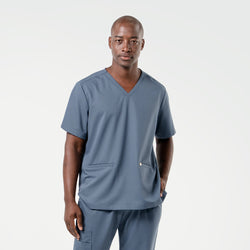 Image of Wearing a Smoky Blue scrub set, the male model stands facing forward with one hand in his pocket, presenting a composed and professional look.