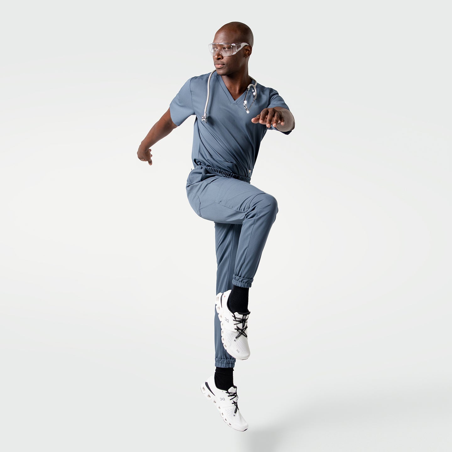 Image of Model in Smoky Blue scrubs wearing a stethoscope, posing dynamically with one knee lifted.