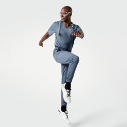 Image of Model in Smoky Blue scrubs wearing a stethoscope, posing dynamically with one knee lifted.