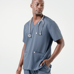 Image of Wearing a Smoky Blue scrub set, the male model looks to the side with one hand in his pocket and a stethoscope draped around his neck.