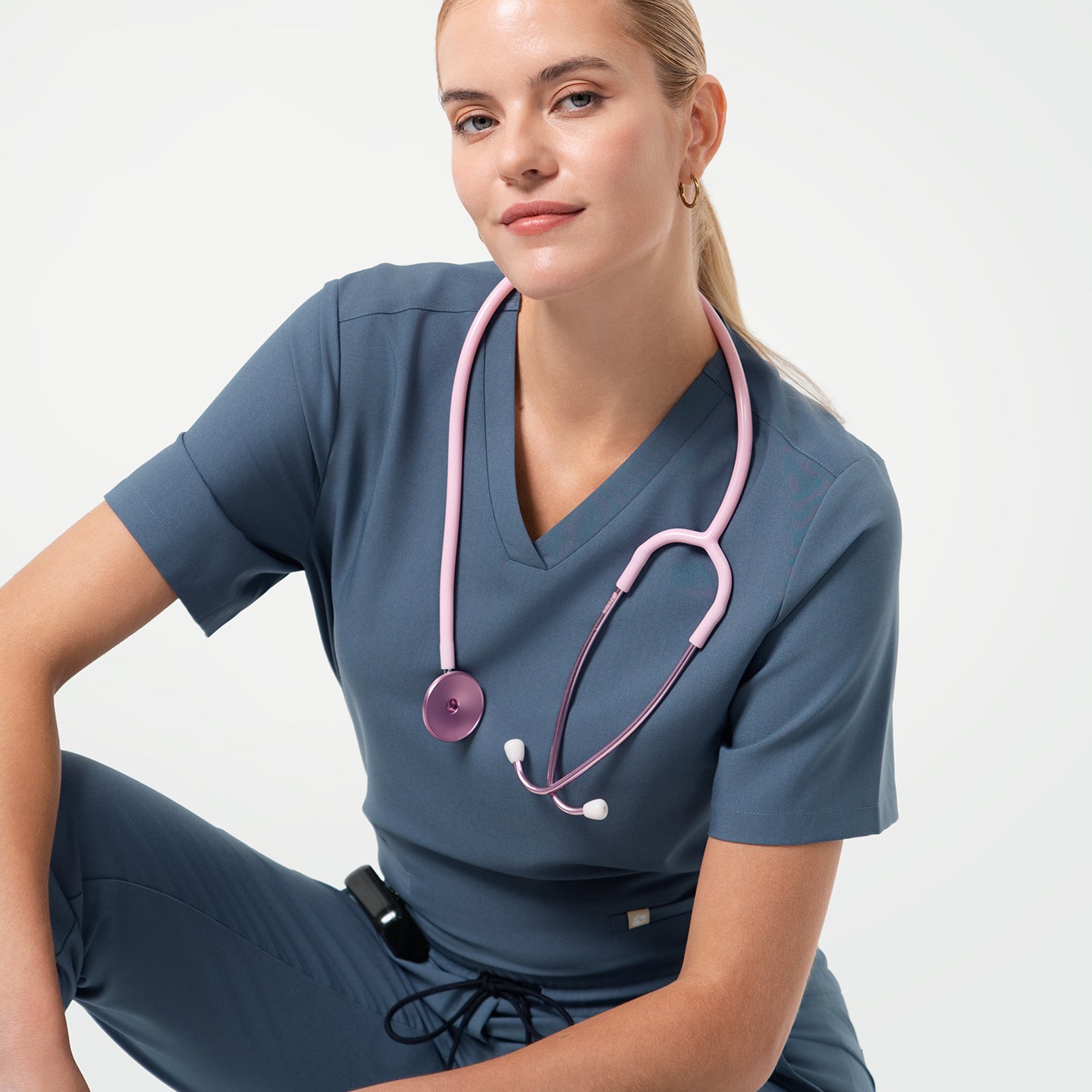 Smiling medical professional poses in Smoky Blue scrub top and matching scrub pants, with a pink stethoscope draped around the neck.